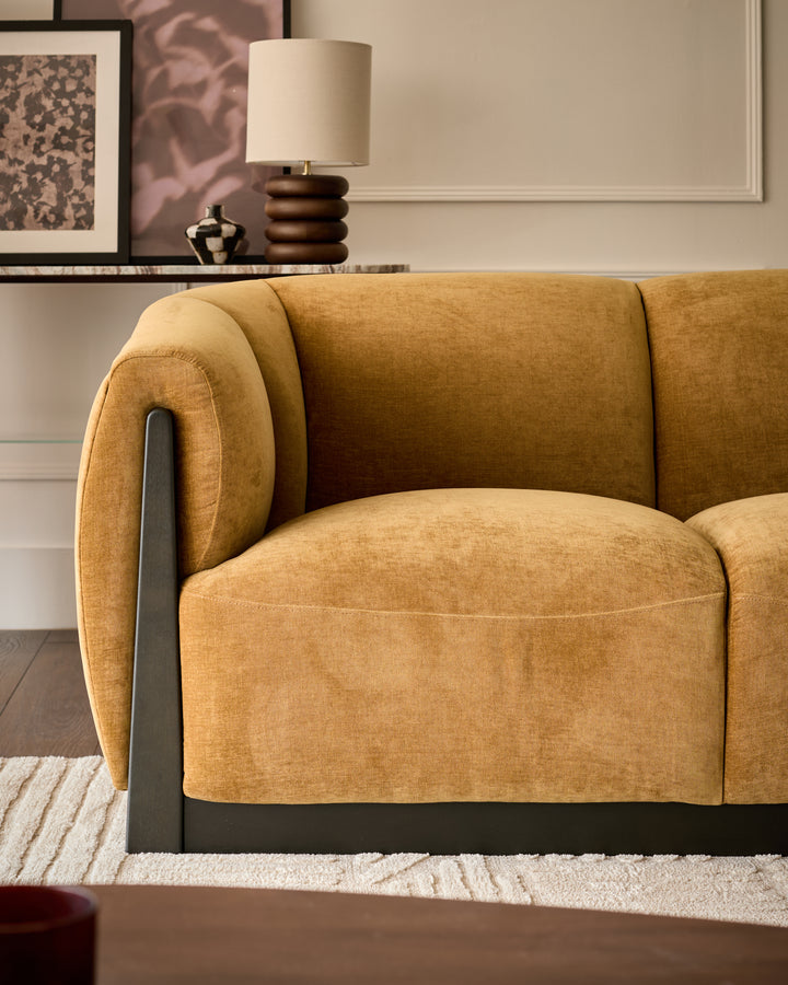 Teagan 2-seater sofa in ochre fabric with curved rolled arms and black metal frame accent, angled side view.