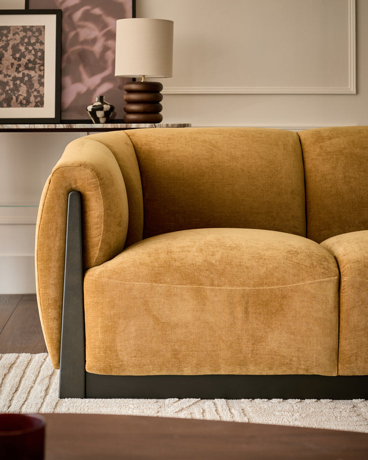 Teagan 2-seater sofa in ochre fabric with curved rolled arms and black metal frame accent, angled side view.
