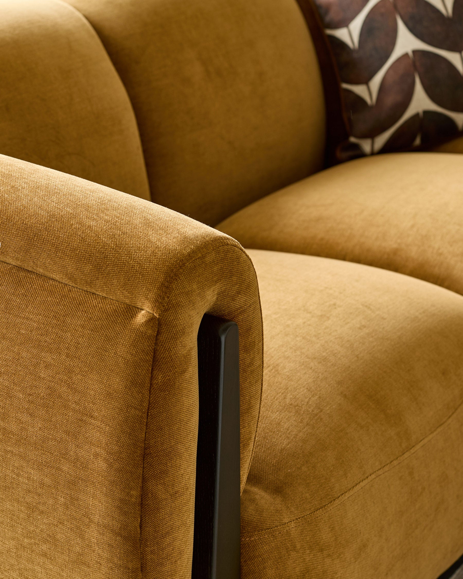 Teagan 3-seater sofa in ochre fabric, showing curved armrest detail with black wooden leg.