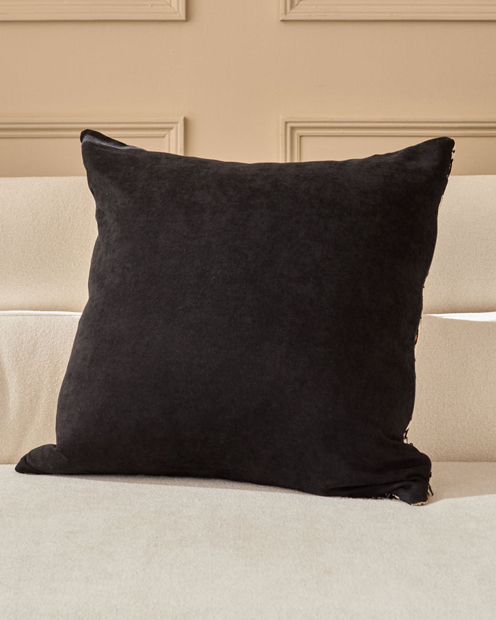Black square cushion with textured fabric displayed on a cream upholstered headboard.