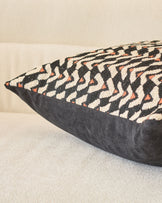 Black cushion with cream and rust geometric patterned fabric top, shown at an angle on neutral surface.