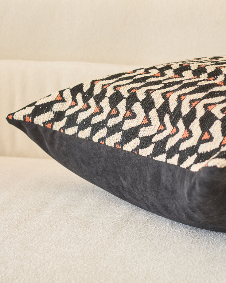 Black cushion with cream and rust geometric patterned fabric top, shown at an angle on neutral surface.