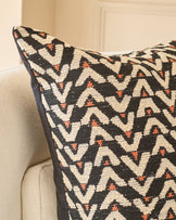 Black and cream geometric patterned cushion with rust orange accents, displayed on a neutral upholstered chair.