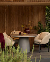 Tesso dark grey round dining table styled outdoors with two cream chairs, wine glasses, and decorative accessories.