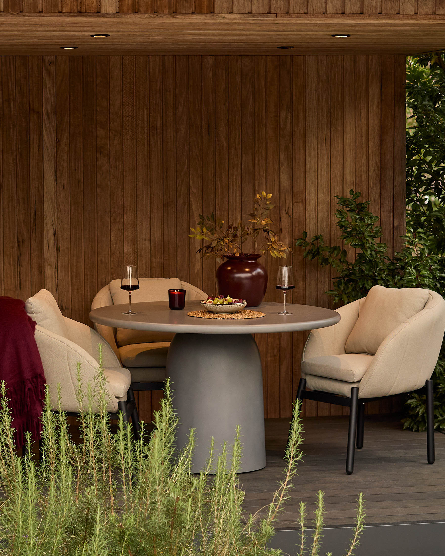 Tesso dark grey round dining table styled outdoors with two cream chairs, wine glasses, and decorative accessories.