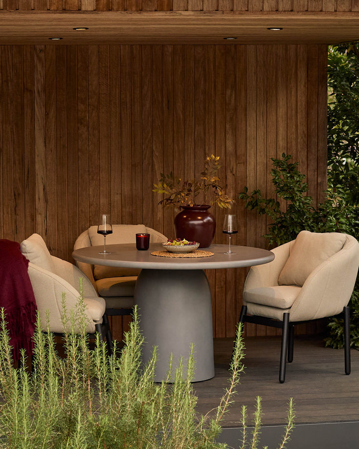Tesso dark grey round dining table styled outdoors with two cream chairs, wine glasses, and decorative accessories.