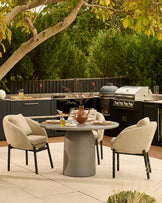Dark grey cylindrical pedestal dining table set with two beige upholstered chairs in modern outdoor setting.