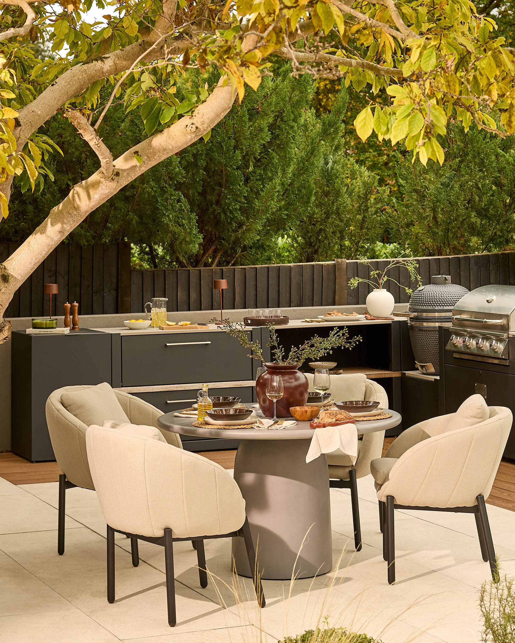 Tesso round dining table with four Camilo chairs in dark grey and natural, styled in outdoor patio setting.