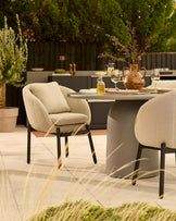 Tesso dark grey dining table with four natural beige Camilo chairs in modern garden setting with greenery and patio.