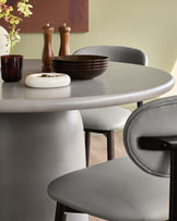 Tesso dark grey round dining table with curved pedestal base, styled with grey chairs and tableware.