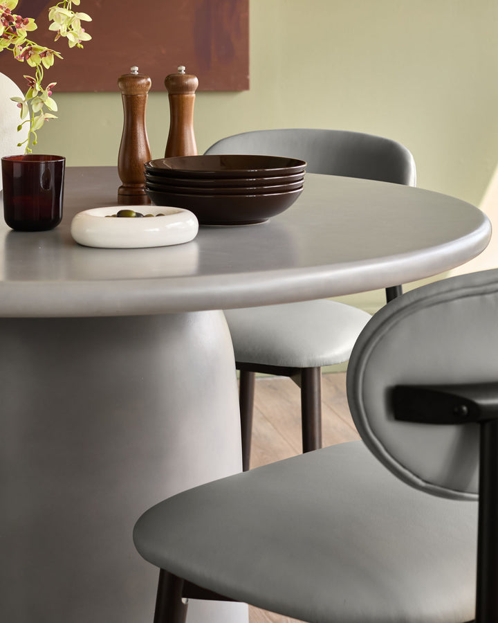 Tesso dark grey round dining table with curved pedestal base, styled with grey chairs and tableware.