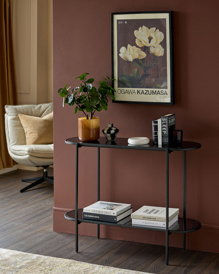 Black oval console table with smoked mirror shelves, displayed in a living room setting with books and decor.