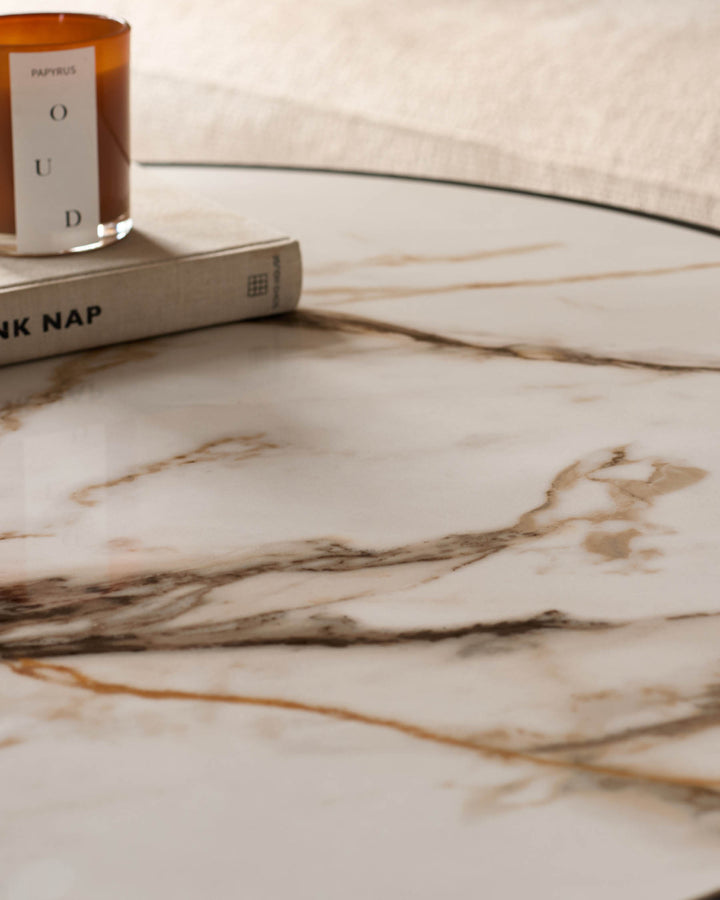 Marble-effect round coffee table styled with a scented candle and decorative book on a neutral surface.