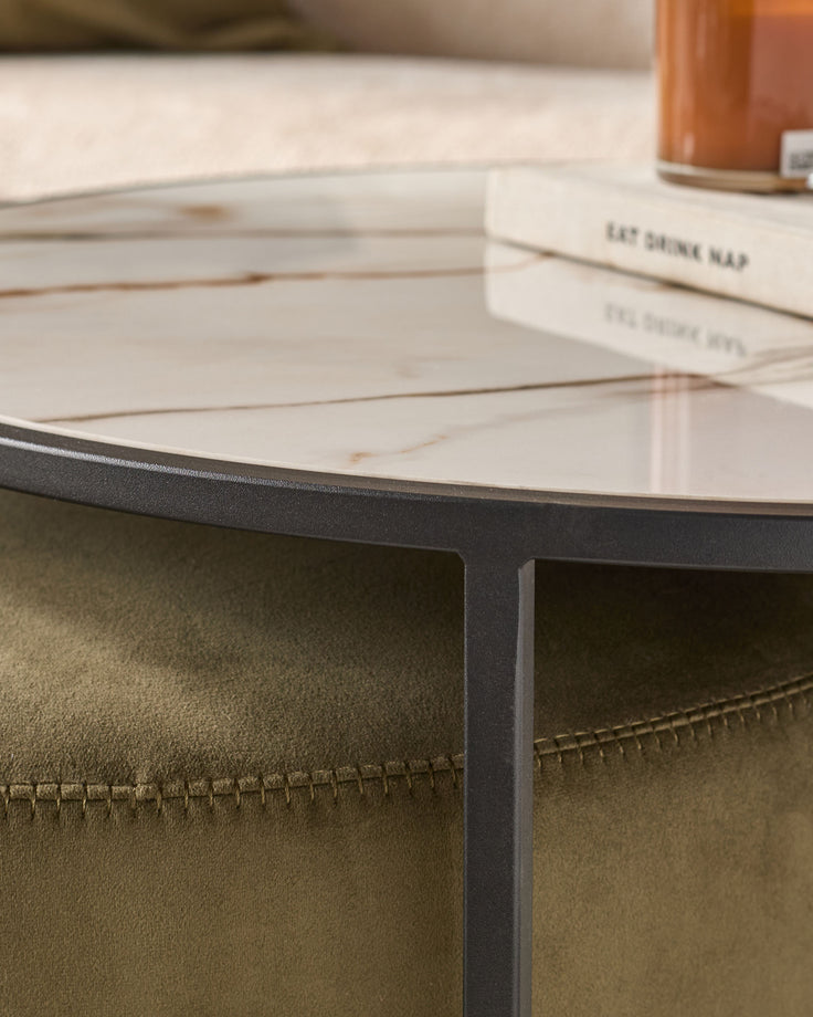 Black round coffee table with white marble top and olive green pouffe with stitched details visible underneath.