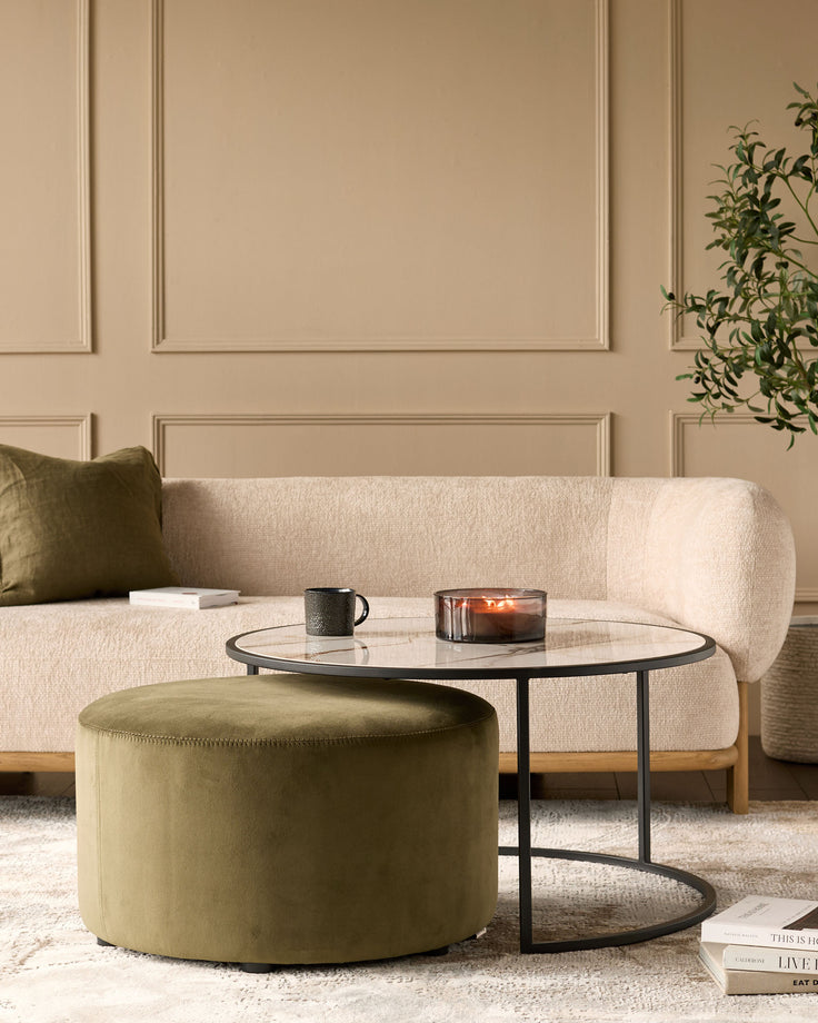Black round coffee table with marble top and olive green upholstered pouffe, styled in modern living room setting.