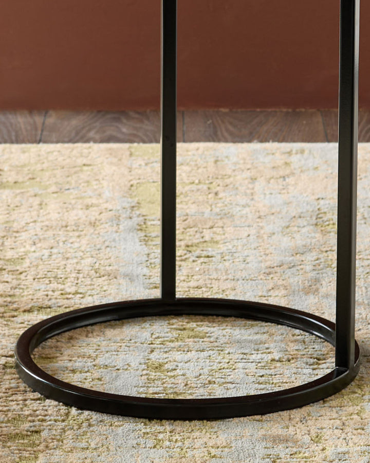 Thea smoked mirror tray table in black with circular base on textured stone floor against brick wall.