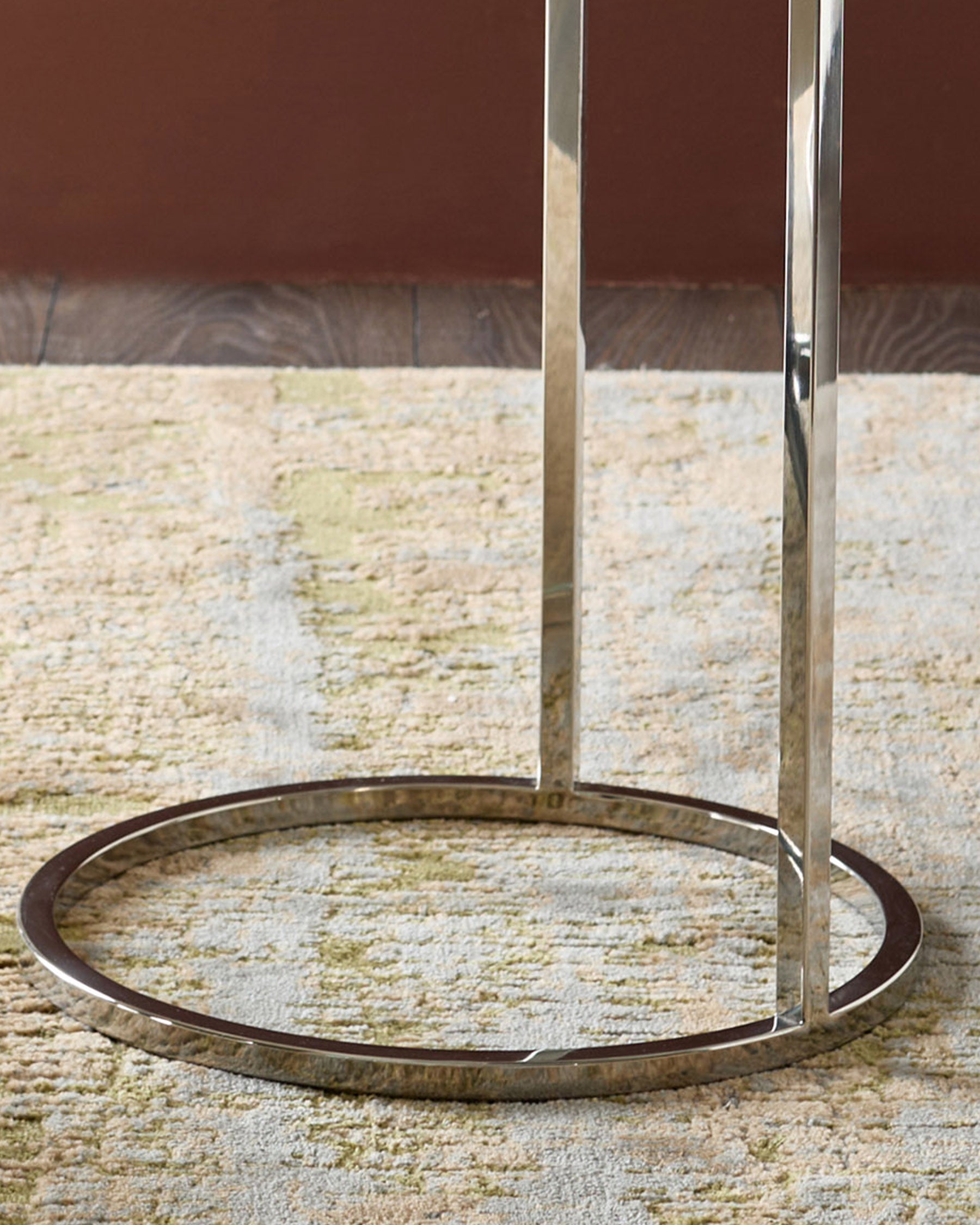 Thea smoked mirror tray table with stainless steel legs on textured stone floor, circular base detail visible.