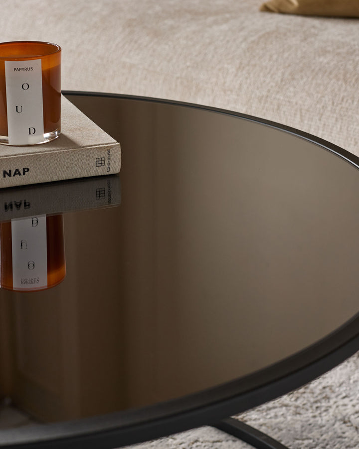 Black round coffee table with cream pouffe, styled with amber candle and book, viewed from above at an angle.