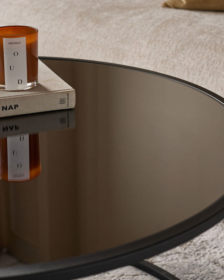 Black round coffee table with cream pouffe, styled with amber candle and book, viewed from above at an angle.