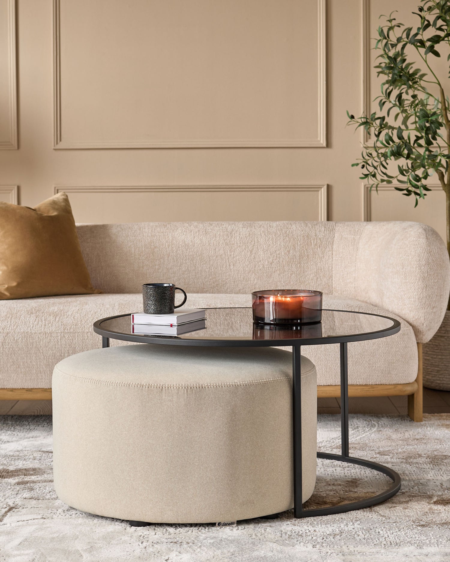 Thea black round coffee table with cream pouffe, styled in a modern living room with beige sofa and accessories.
