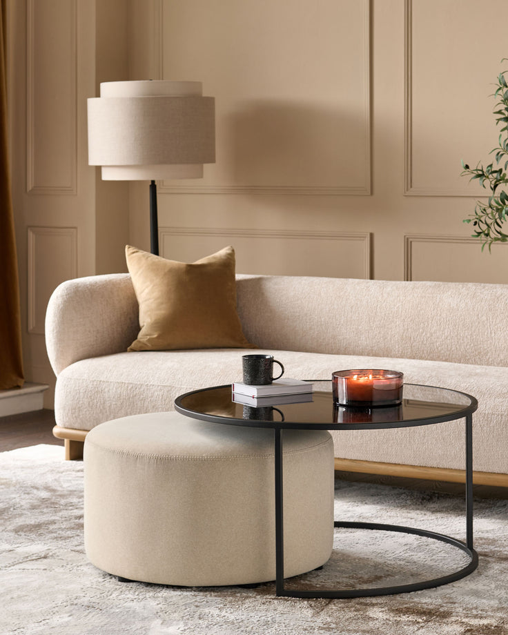 Thea black round coffee table and cream pouffe set in a modern living room setting.