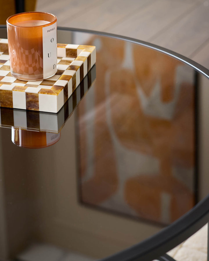 Black round coffee table with grey top featuring a checkered decorative box and orange candle, reflecting in the glossy surface.