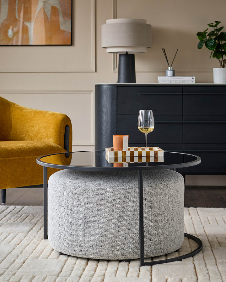 Black round coffee table with grey upholstered pouffe base, styled in modern living room setting.