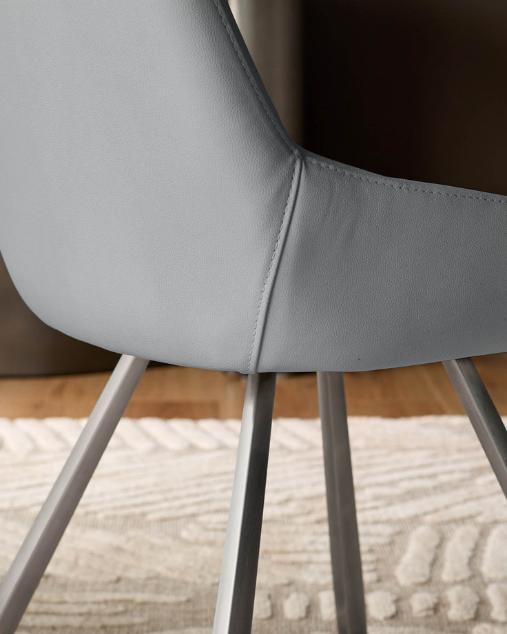 Theo mid-grey faux-leather dining chair, angled view showing curved seat back and metal legs on light rug.