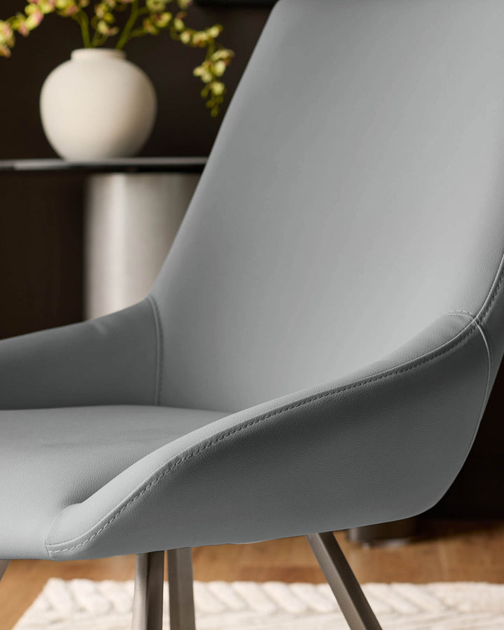 Theo mid-grey faux-leather dining chair, side angle view showing curved backrest and stitched details on seat.