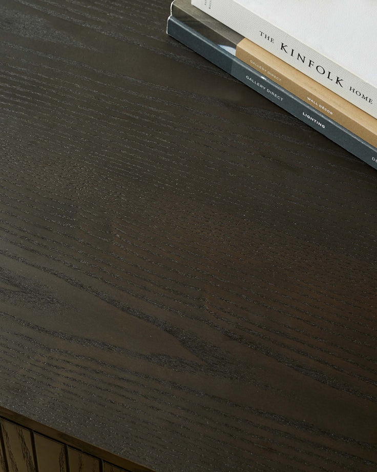 Close up of a dark wood table with books on top, featuring a subtle grain pattern.