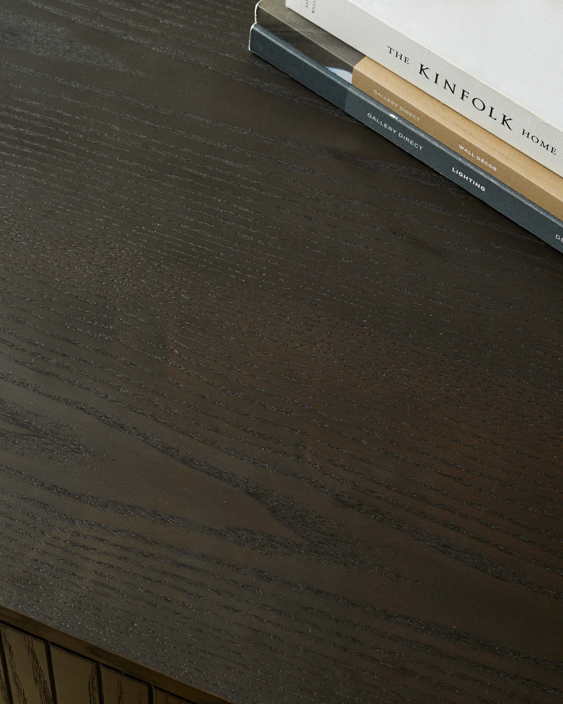 A dark wood furniture surface with the books 'The Kinfolk Home' and 'Gallery Direct Lighting' on display.