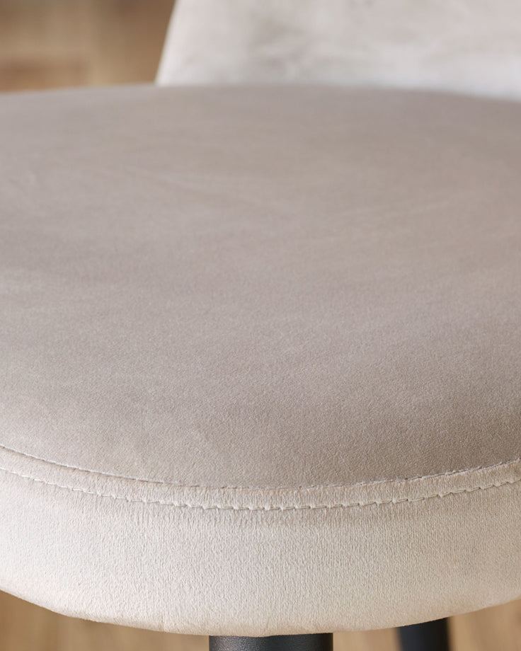 Champagne velvet dining chair close-up showing soft upholstered seat and stitched seam detail.