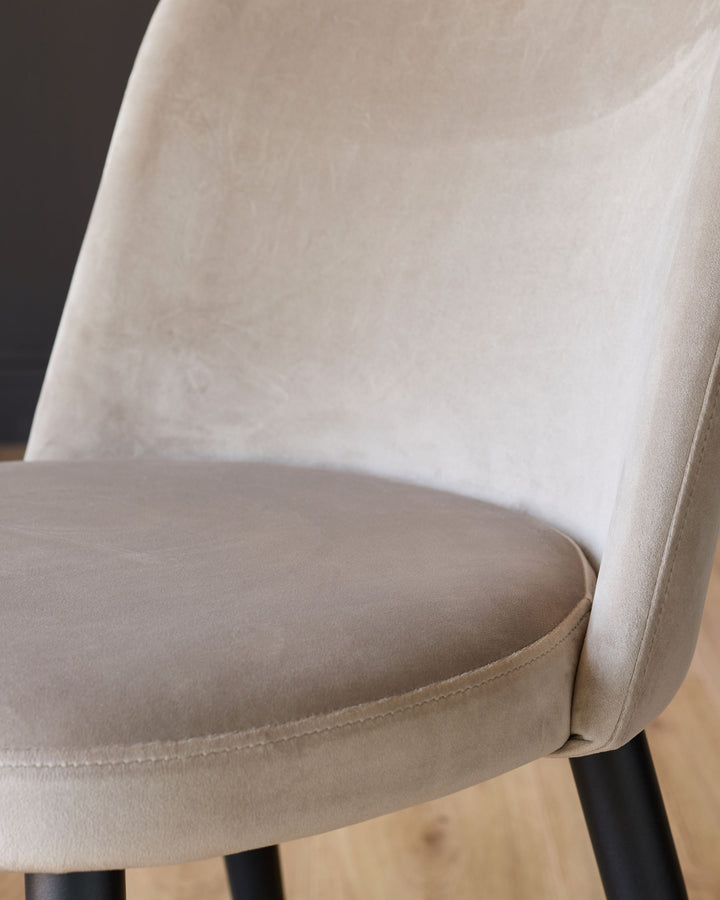 Trinny velvet dining chair in champagne, side angle detail showing curved backrest and seat cushion with black legs.