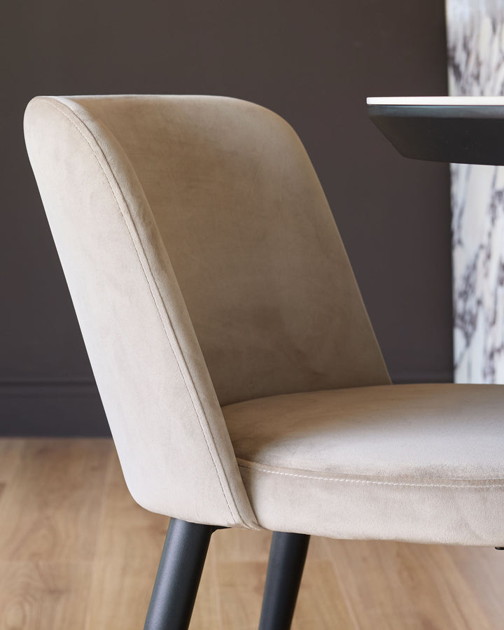 Champagne velvet dining chair with curved backrest and black legs, angled side view on wooden floor.