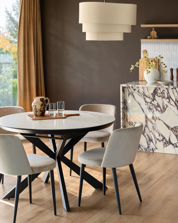 Champagne velvet dining chair with black tapered legs, shown in a styled dining room setting around a round marble table.