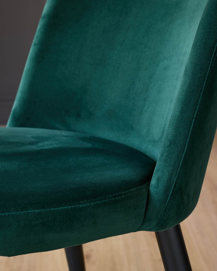 Dark green velvet dining chair with curved backrest and black legs, close-up detail view.