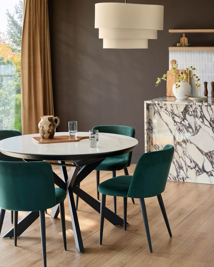 Dark green velvet dining chair with black legs, shown in modern dining room setting around white marble table.