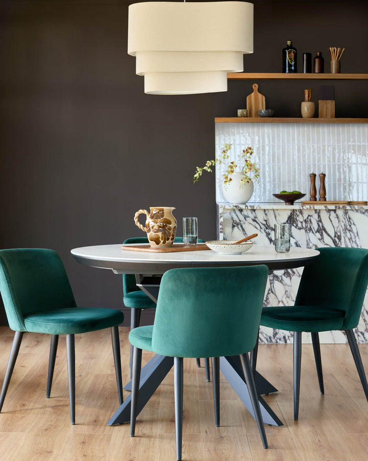 Trinny velvet dining chair in dark green, shown in a styled dining room setting around a white round table.