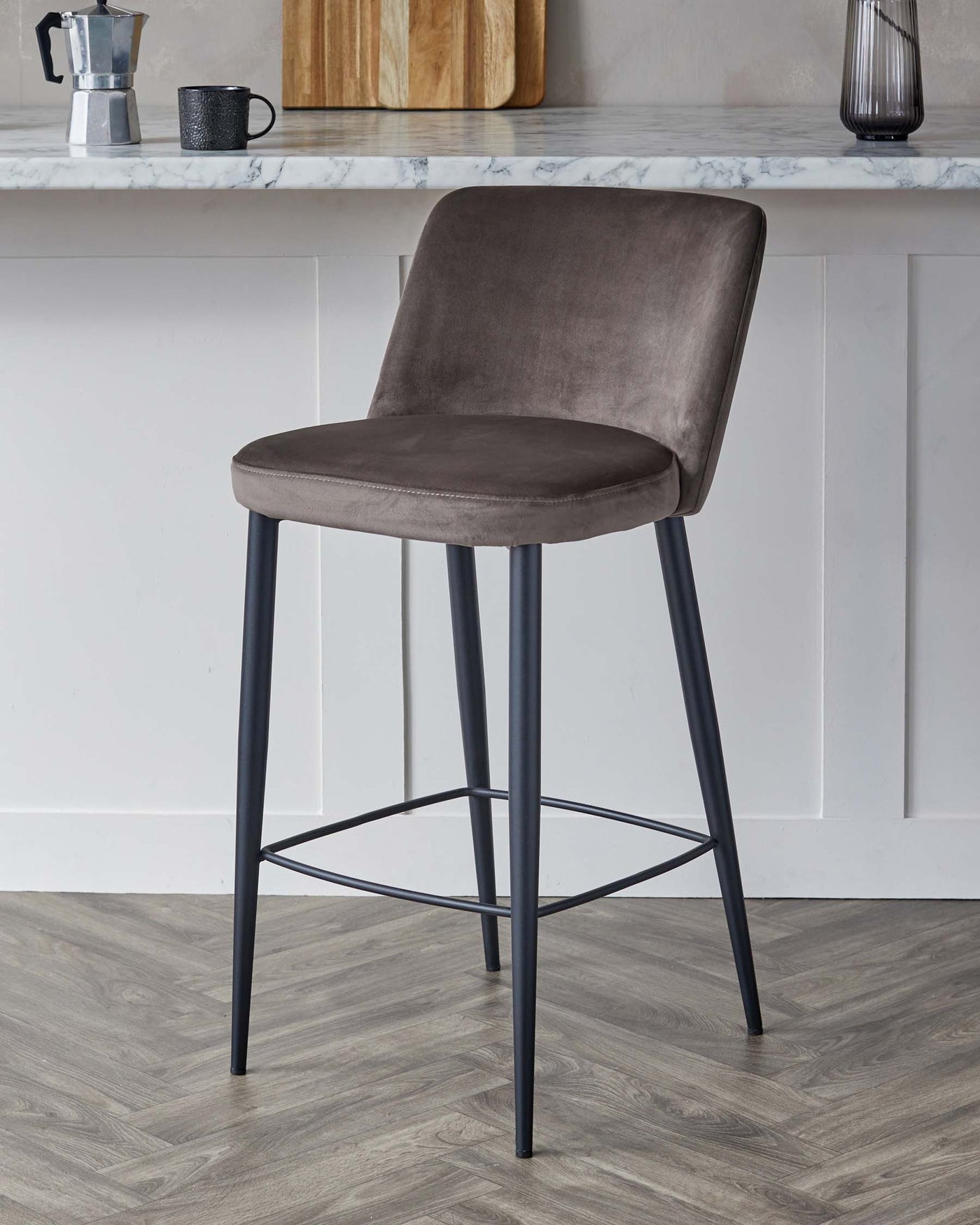 Contemporary bar stool featuring a curved back, cushioned seat upholstered in grey velvet fabric, and sleek black metal legs with a footrest.