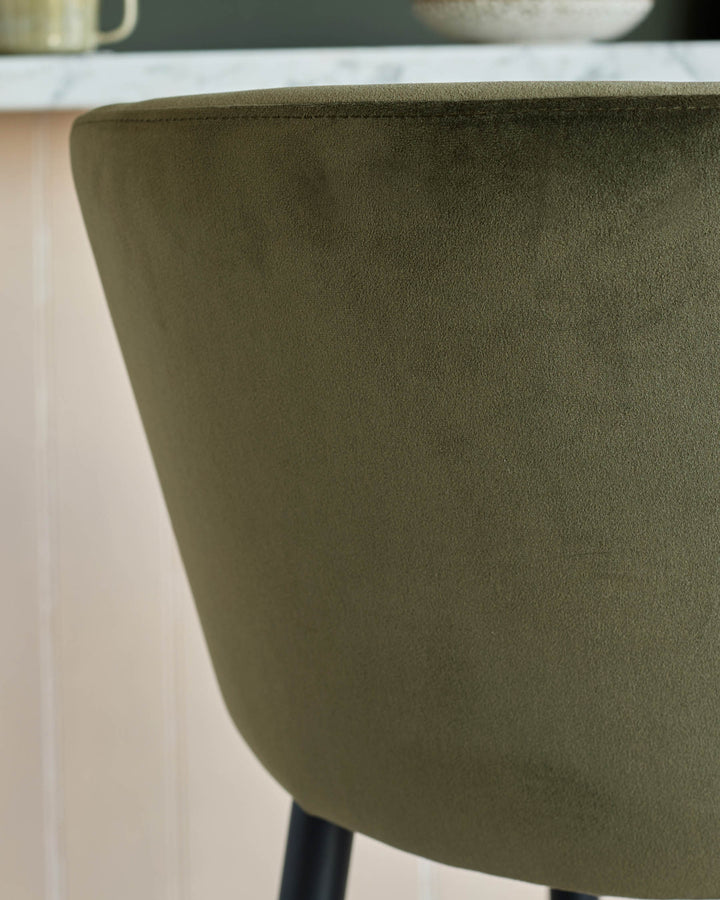 Close-up of an olive-green velvet chair back, showing the textured fabric and minimalist design.