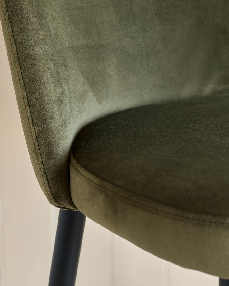 Close up of an olive green chair with black legs, showcasing its plush velvet fabric and sleek design.