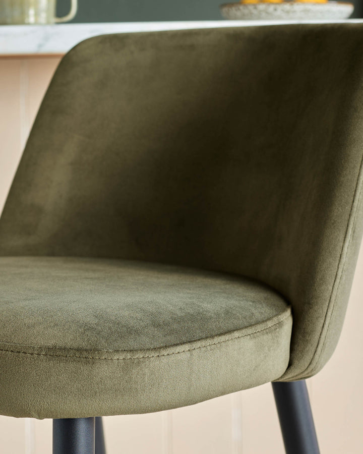 Close up of a green velvet chair with black legs, showcasing its plush fabric and modern design.