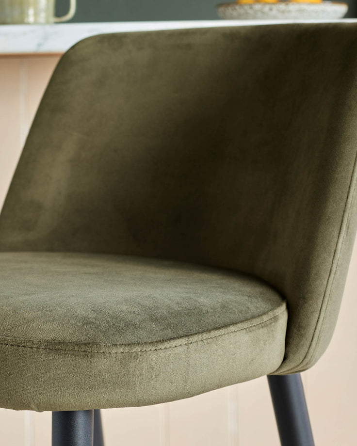 Close up of a green velvet chair with black legs, showcasing its plush fabric and modern design.