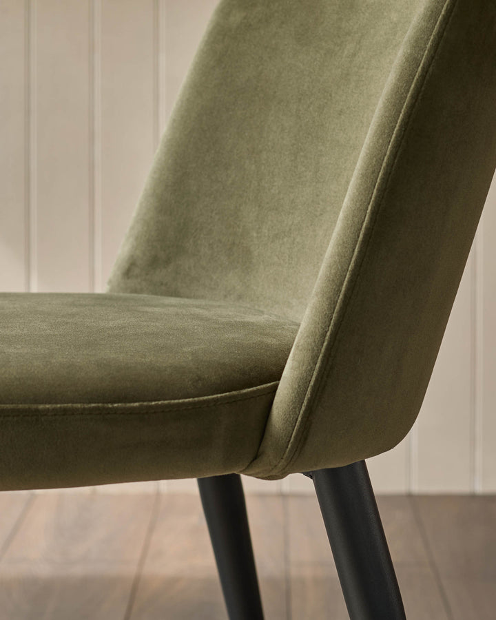 Close-up of a green velvet chair showing the seat, backrest, and black metal legs. Modern furniture design.