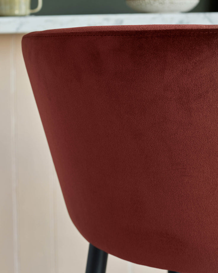 Close-up of a stylish chair upholstered in a deep burgundy, textured fabric, with a clean, modern design and dark legs.