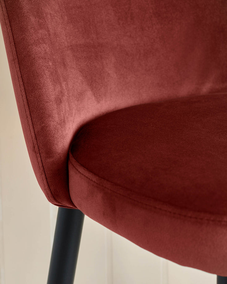 Close-up of a plush red velvet chair with sleek black legs, showcasing its luxurious texture and modern design.
