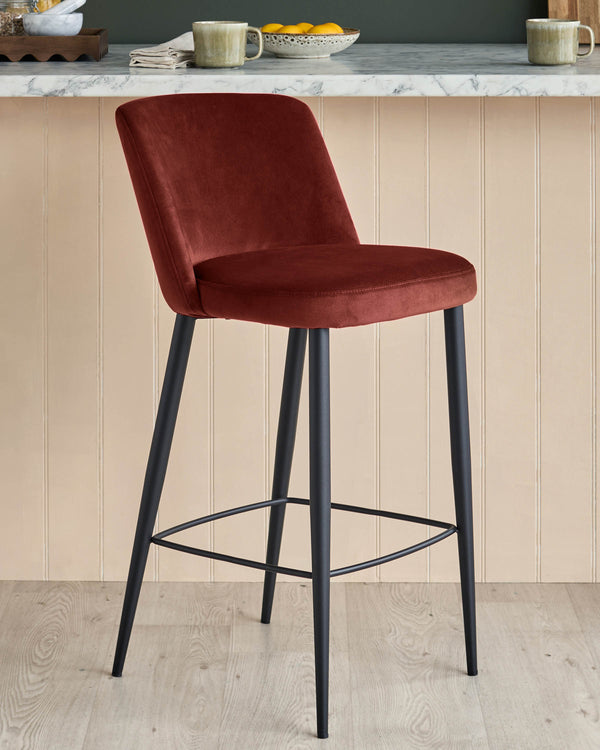 A plush, burgundy velvet bar stool with black metal legs sits invitingly in front of a neutral kitchen counter.