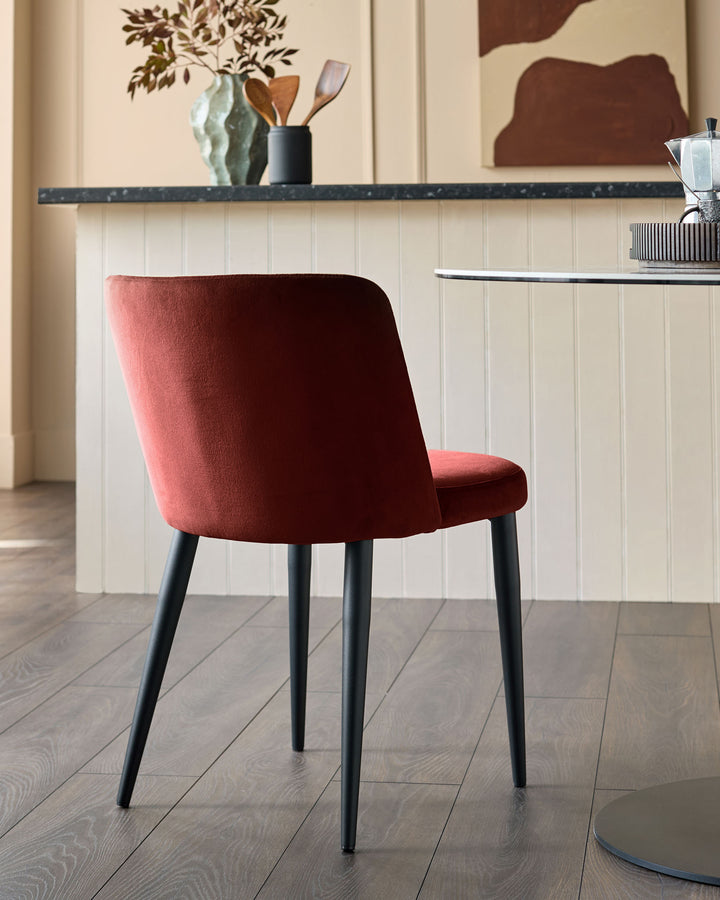 Close-up of a red velvet dining chair with black legs, set against a kitchen background with a round table.