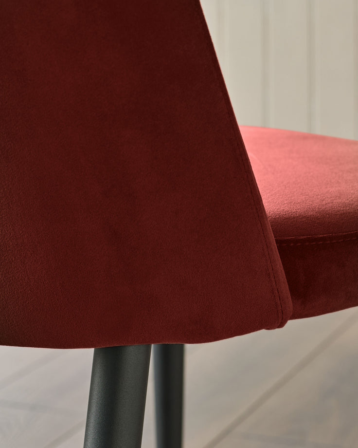 Close-up of a stylish red velvet chair with black legs, showcasing modern design and luxurious comfort.