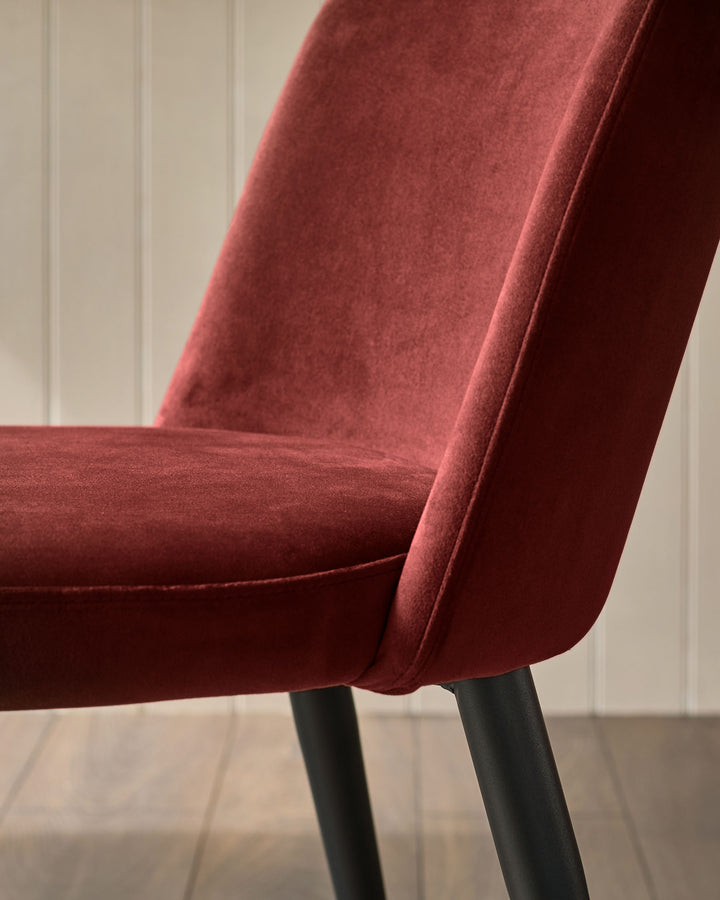 Close-up of a stylish, luxurious-looking red velvet chair with black legs. Modern and comfortable seating.